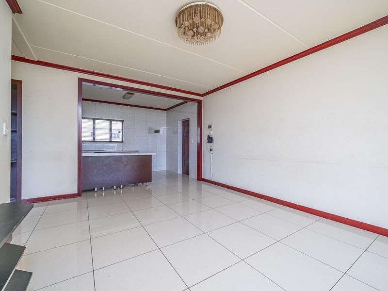 An open-plan living and kitchen area featuring tiled flooring, neutral walls with red trim, and a functional kitchen layout.