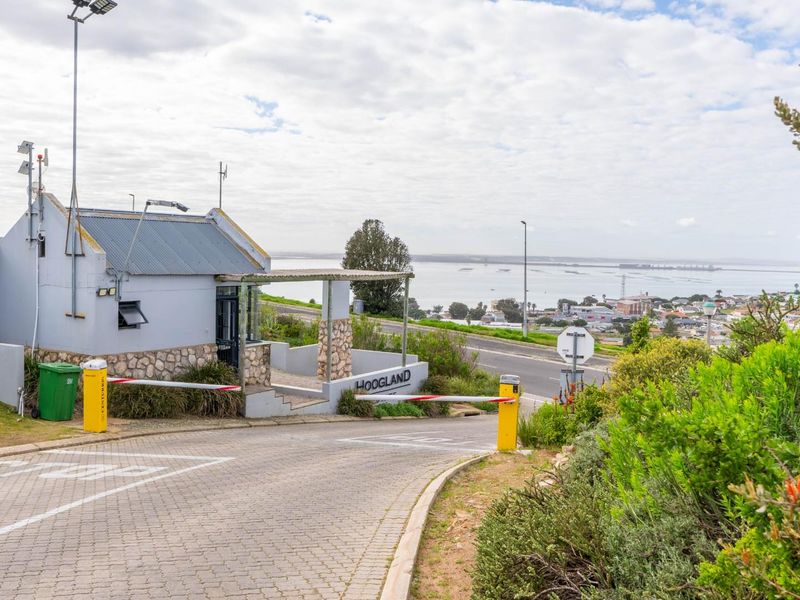 Entrance to the residential estate featuring a security boom gate, guard house, and paved driveway with views of the surrounding area.