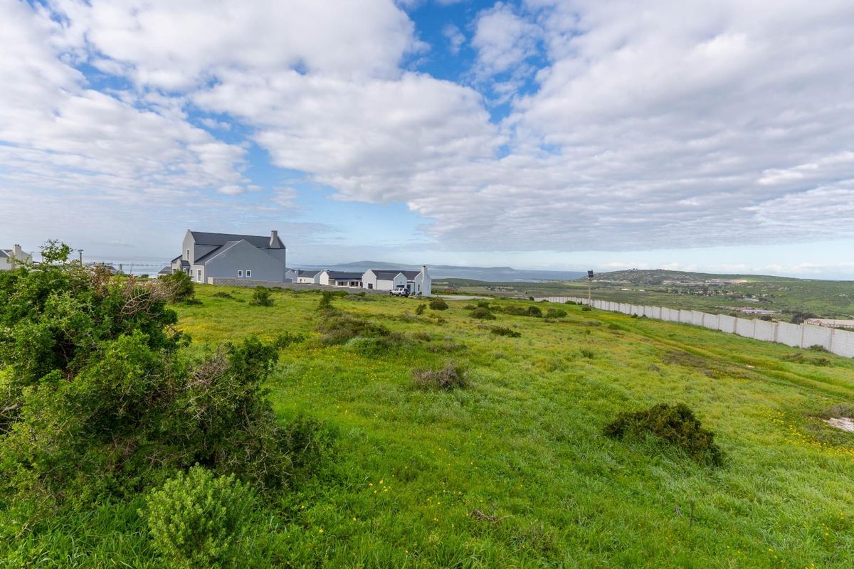 A wide-angle view of a vacant residential plot featuring natural vegetation, perimeter fencing, and surrounding neighborhood homes in the distance.
