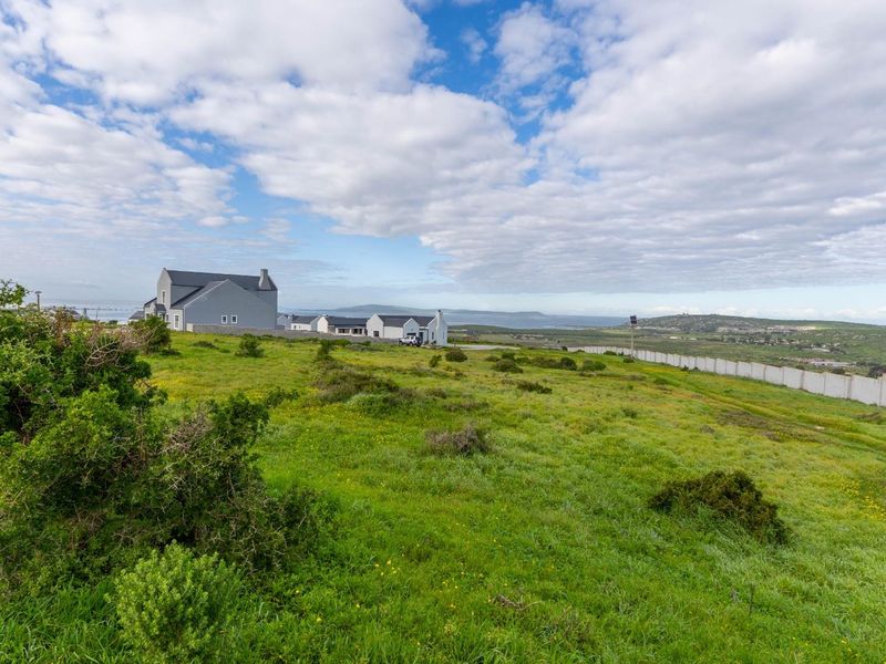 A wide-angle view of a vacant residential plot featuring natural vegetation, perimeter fencing, and surrounding neighborhood homes in the distance.