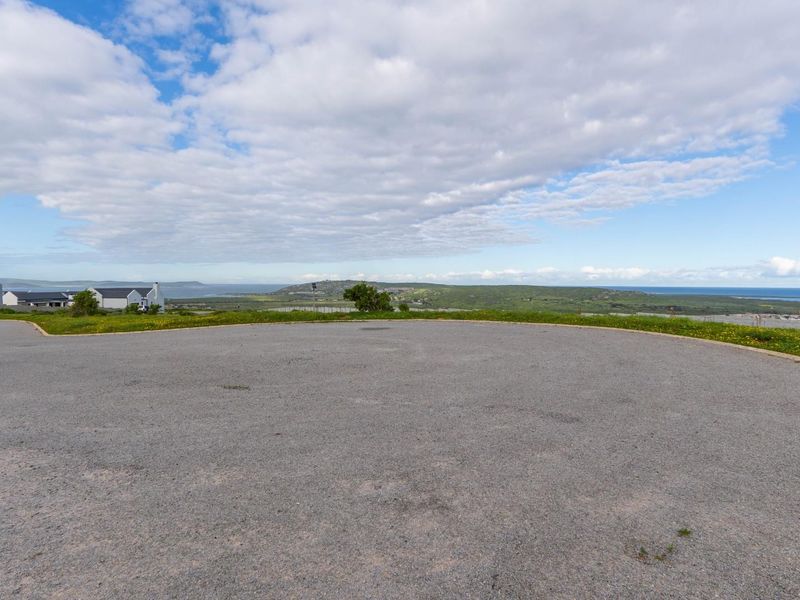 A wide-angle view of the vacant residential land featuring a paved driveway area with expansive coastal and landscape views in the background.
