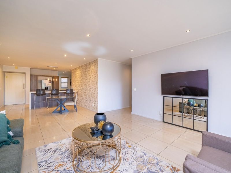 Spacious open-plan living and kitchen area featuring modern porcelain floor tiles, recessed lighting, and a stylish textured feature wall.