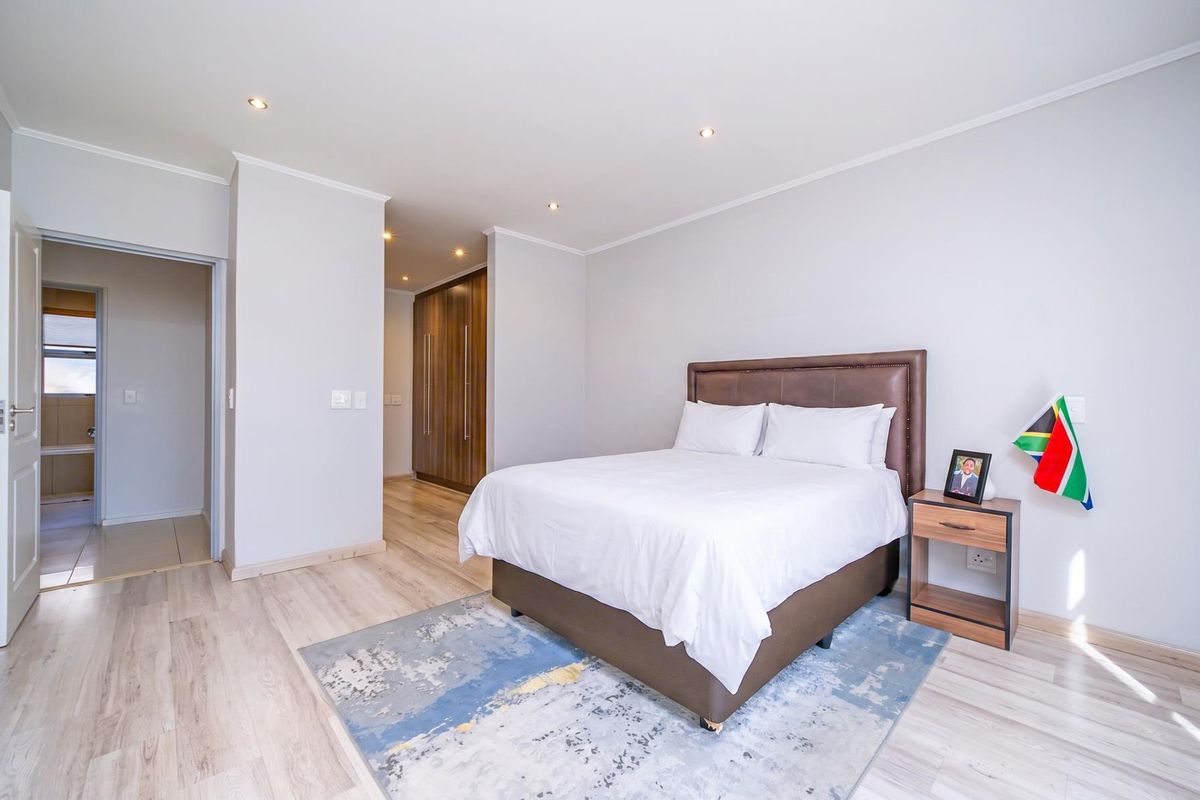 A well-maintained bedroom featuring light laminate flooring, recessed downlighting, and ample built-in cupboard space, leading to an adjoining bathroom area.