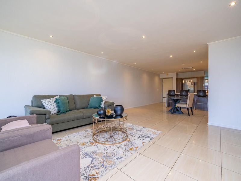 Spacious open-plan living and dining area featuring neutral tiled flooring, recessed downlighting, and a modern kitchen with a breakfast island.