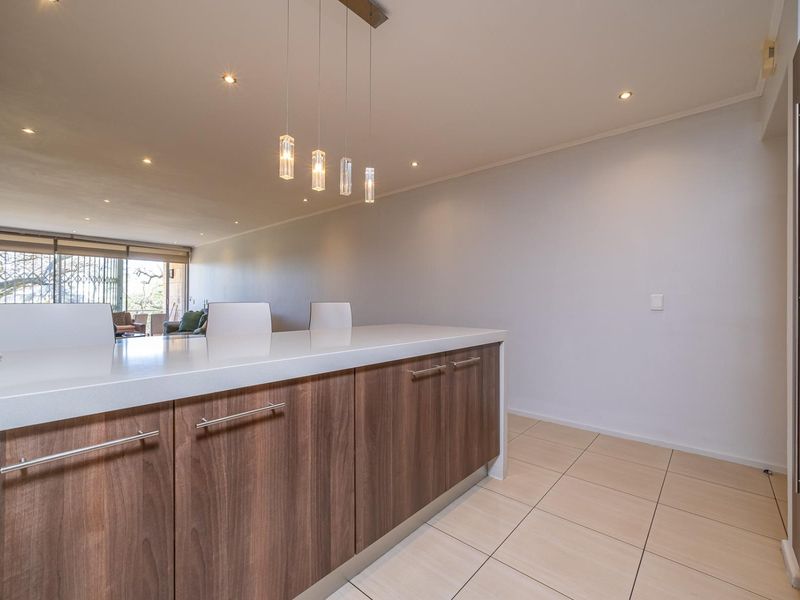 Modern open-plan kitchen area featuring a central island with stone countertops, wood-finish cabinetry, and contemporary pendant lighting, flowing into the adjacent living space.