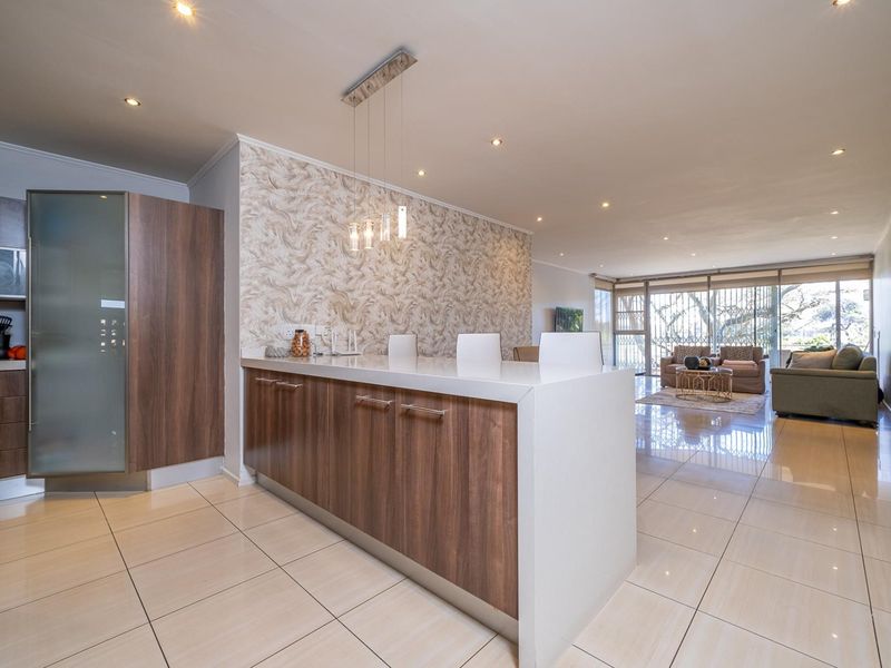 Modern open-plan living area featuring a sleek kitchen island with stone countertops, tiled flooring, and seamless flow to the adjacent lounge and balcony.