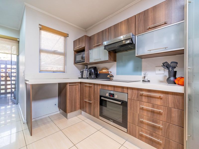 Modern kitchen featuring wood-finish cabinetry, stone countertops, integrated oven, hob, and extractor fan, with tiled flooring and a glass splashback.