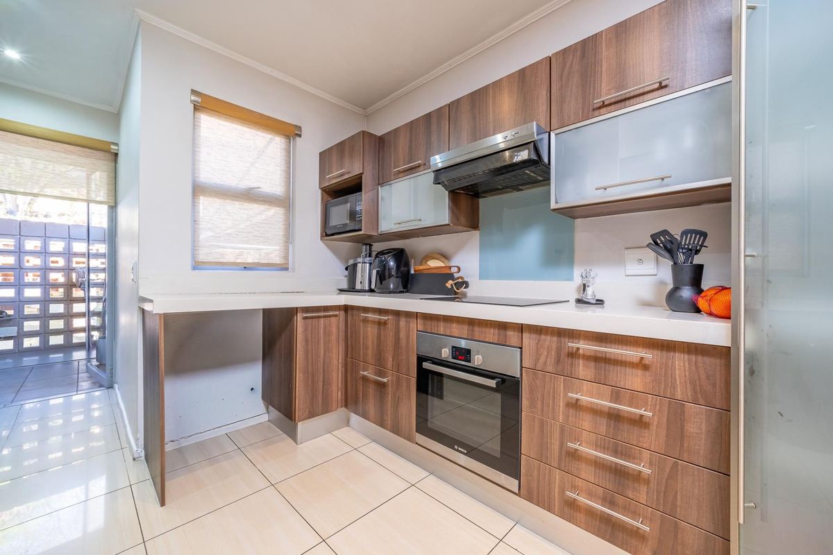 Modern kitchen featuring wood-finish cabinetry, stone countertops, integrated oven, hob, and extractor fan, with tiled flooring and a glass splashback.