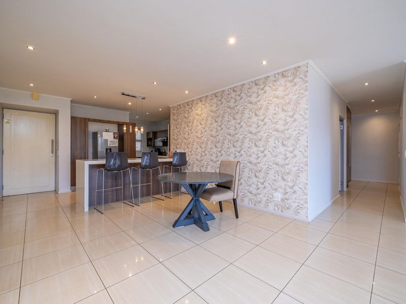 Open-plan living area featuring tiled floors, recessed lighting, a kitchen island with breakfast bar, and a decorative wallpaper feature wall.