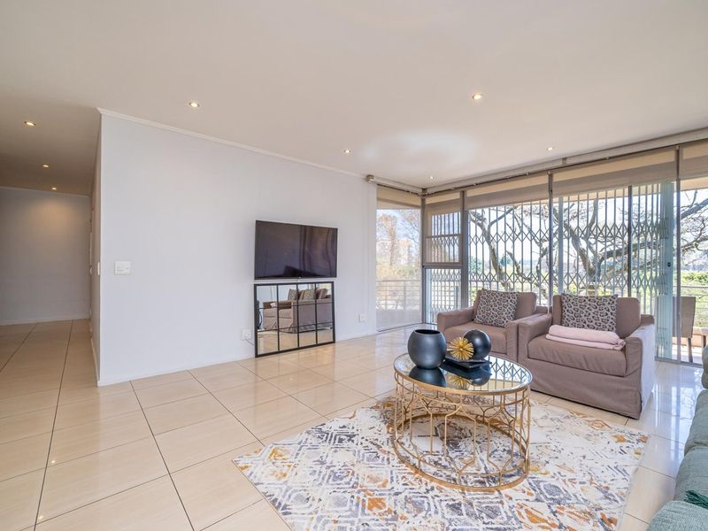A bright and spacious living room featuring neutral tiled flooring, recessed downlights, and large sliding glass doors with integrated security gates.
