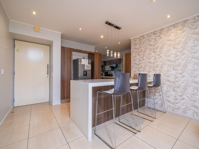 Modern open-plan kitchen featuring a central island with breakfast bar seating, sleek cabinetry, and contemporary pendant lighting, set against a decorative feature wall.
