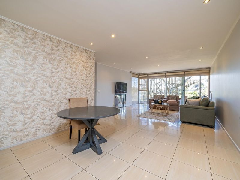 Spacious open-plan living and dining area featuring polished tile flooring, recessed lighting, and a decorative feature wall with access to a balcony.