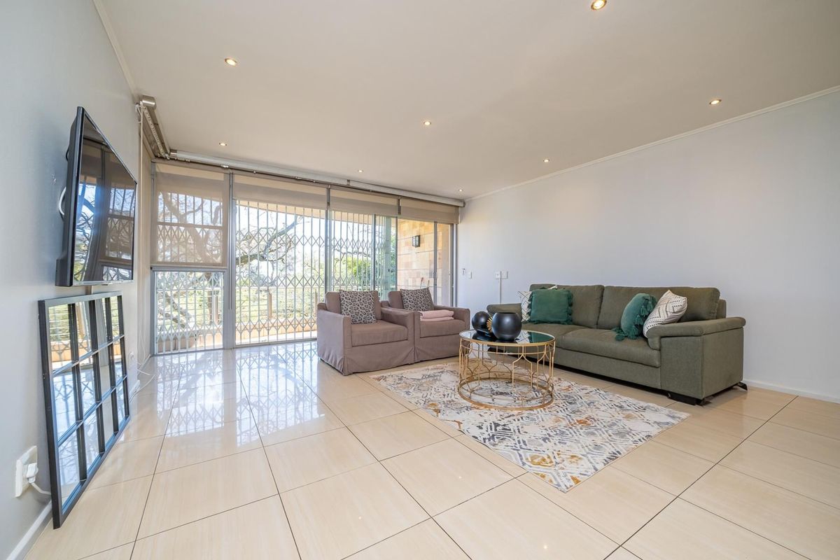 A bright and spacious living room featuring polished tiled flooring, recessed downlighting, and large sliding glass doors leading to an outdoor area.