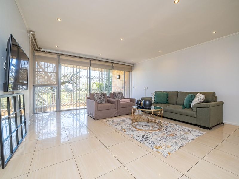 A bright and spacious living room featuring polished tiled flooring, recessed downlighting, and large sliding glass doors leading to an outdoor area.