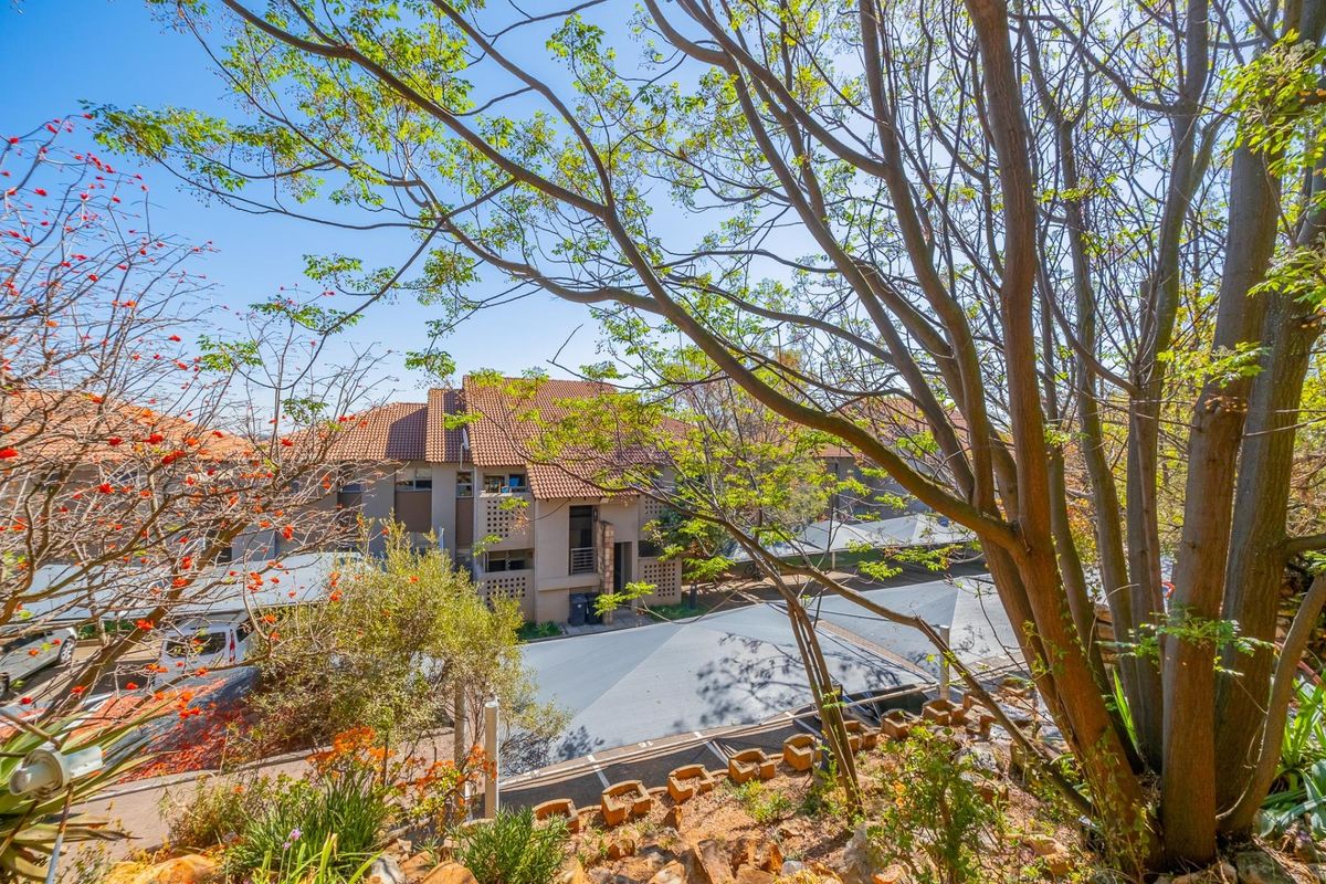 View of the apartment complex exterior featuring terracotta tiled roofs, established trees, and covered carport parking bays.