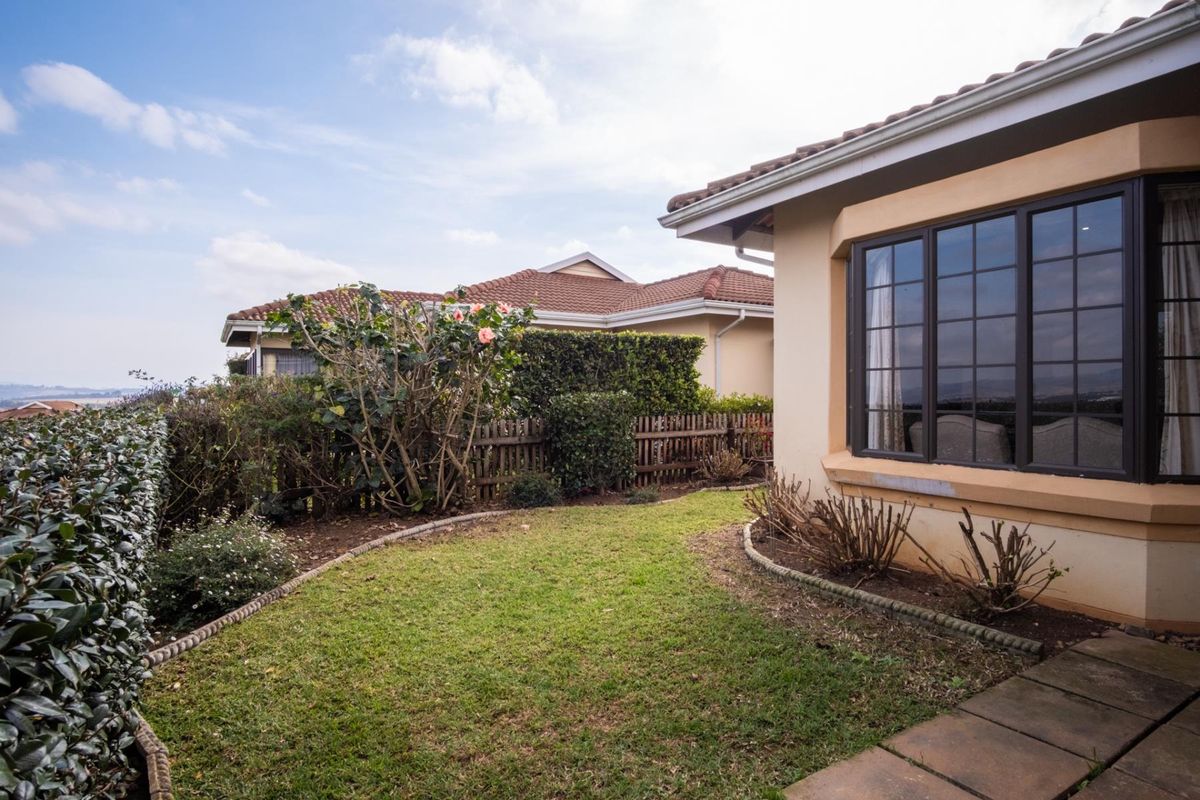 A view of the rear garden featuring a lawn, paved pathway, and bay window, set against a backdrop of neighboring townhouse properties.