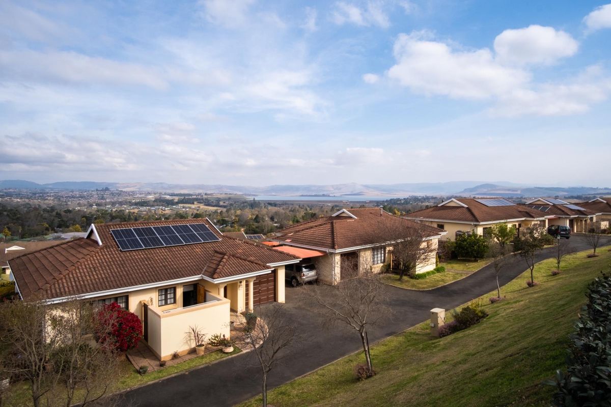 Aerial view of a townhouse complex featuring tiled roofs, solar panel installations, paved driveways, and scenic landscape views.