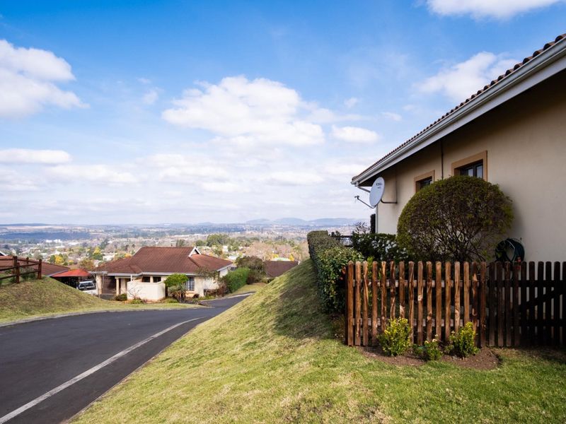 A view of the townhouse exterior featuring a tiled roof, picket fence, and paved driveway, overlooking the surrounding neighborhood and landscape.