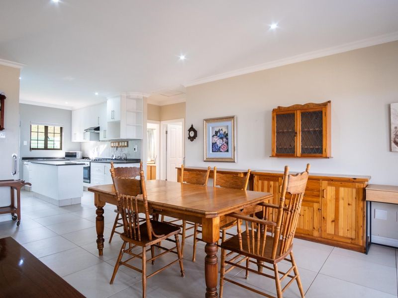 Open-plan dining area flowing into a modern kitchen with white cabinetry, tiled floors, and recessed lighting.