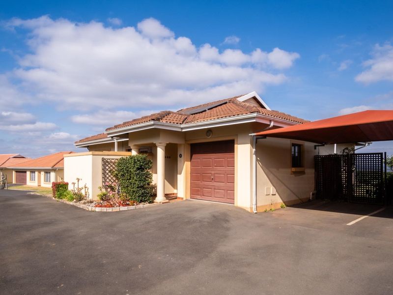 Front elevation of a townhouse featuring a tiled roof, integrated garage, and a covered carport area with paved driveway access.