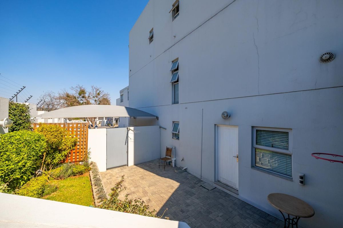 Rear exterior view of the townhouse featuring a paved patio area, shade sail, and a small landscaped garden section.