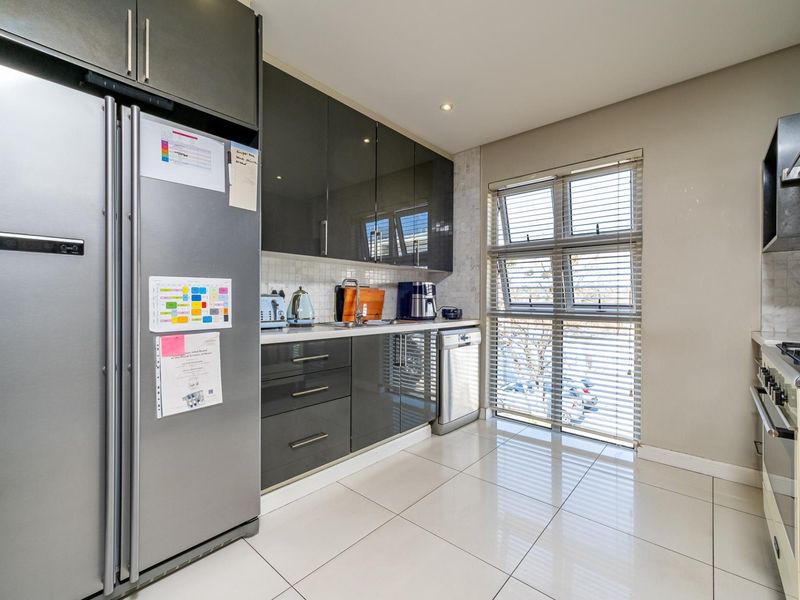 Modern kitchen featuring high-gloss cabinetry, tiled backsplash, built-in gas hob with extractor fan, and sleek tiled flooring.