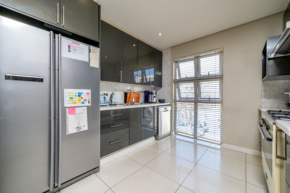 Modern kitchen featuring high-gloss cabinetry, tiled backsplash, built-in gas hob with extractor fan, and sleek tiled flooring.