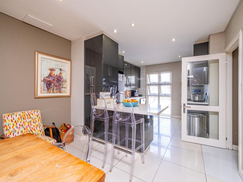 Modern open-plan kitchen featuring high-gloss cabinetry, stone countertops, and a breakfast bar, seamlessly integrated with the dining area and tiled flooring.