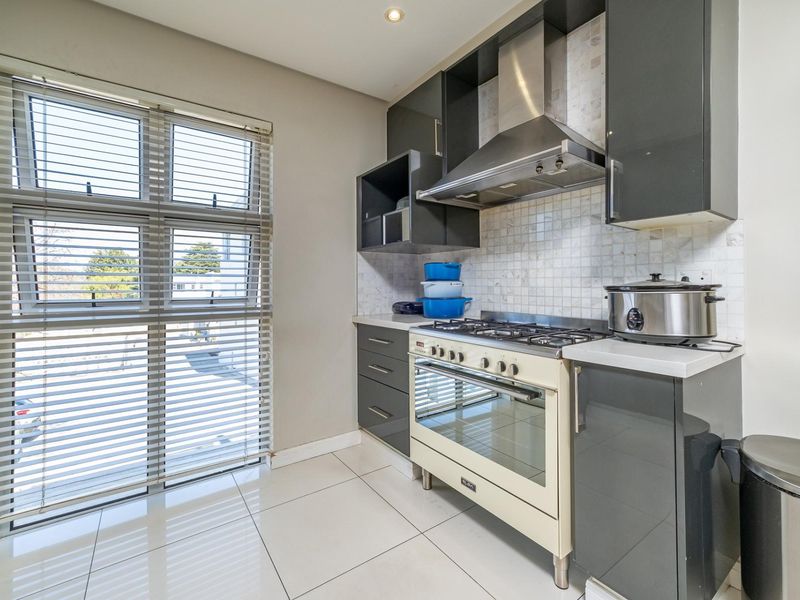 Modern kitchen featuring dark grey cabinetry, stone countertops, a gas stove with extractor fan, and a mosaic tile backsplash with large format floor tiles.