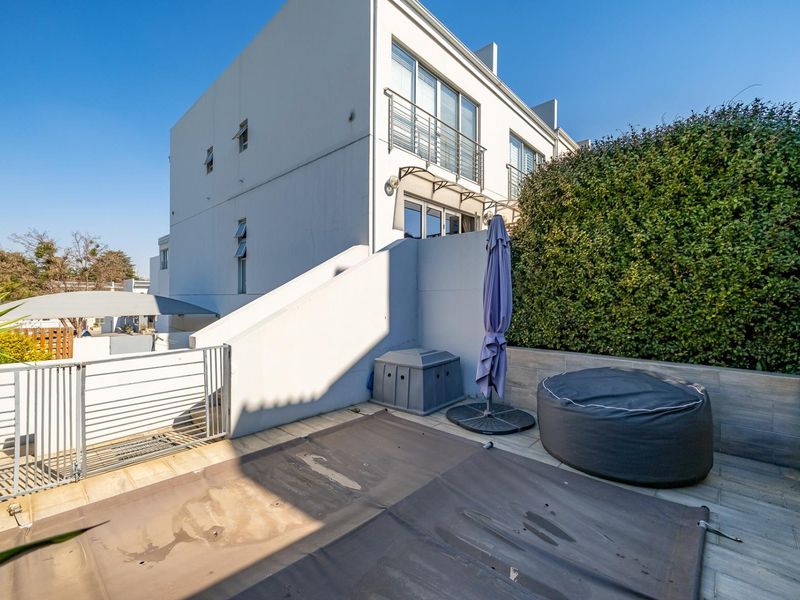 A paved outdoor patio area featuring a retaining wall, metal balustrade, and access to an external staircase, suitable for outdoor living.
