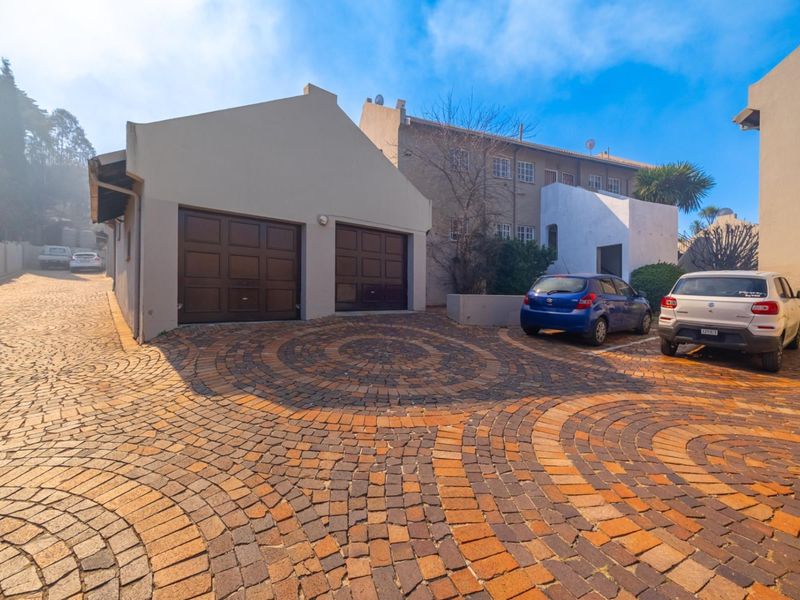 Front exterior view of the townhouse featuring a double garage with sectional doors and a decorative paved driveway.