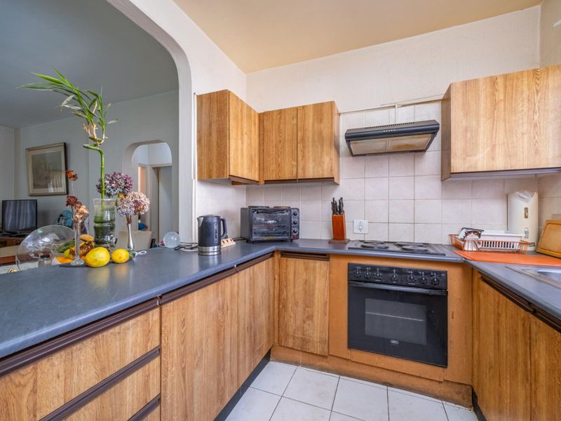 A functional kitchen featuring wood-look laminate cabinetry, dark countertops, built-in oven, and hob, with an open-plan layout connecting to the living area.