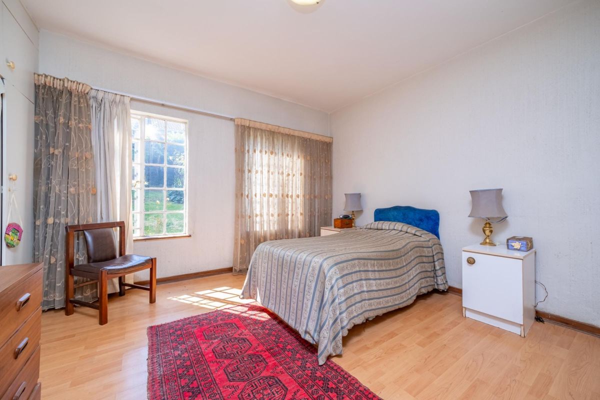 A bedroom featuring laminate flooring and a multi-pane window with curtain tracks, offering a functional space with natural light.