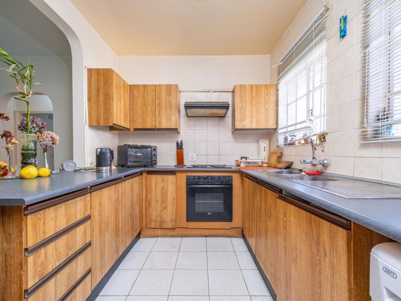 A functional U-shaped kitchen featuring wood-look laminate cabinetry, built-in oven, electric hob, and tiled finishes, offering a classic layout ready for modern updates.