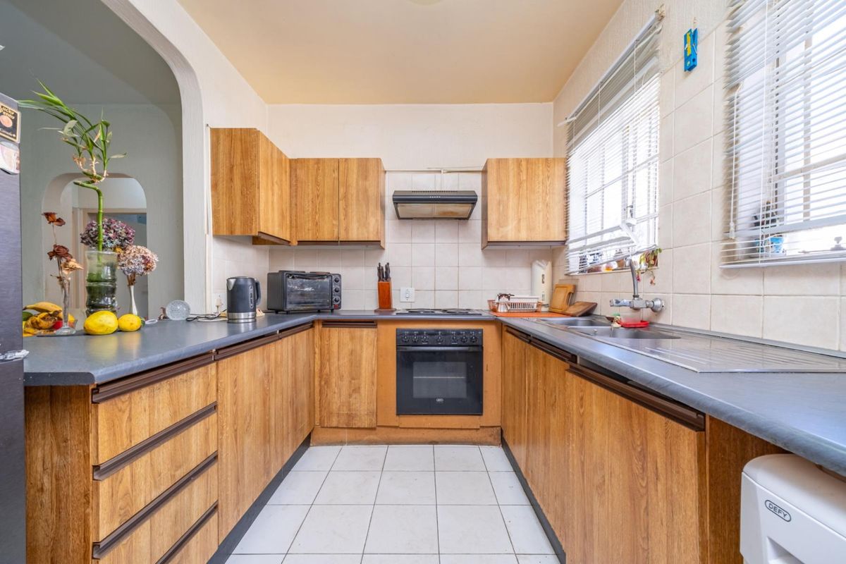 A functional U-shaped kitchen featuring wood-look laminate cabinetry, built-in oven, electric hob, and tiled finishes, offering a classic layout ready for modern updates.