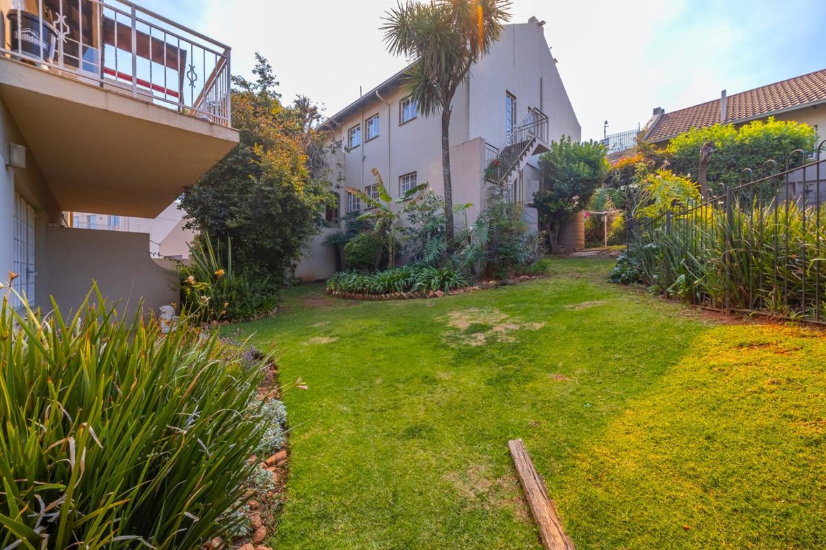A rear view of the townhouse featuring a private garden, lawn area, and an external staircase leading to an upper-level balcony.
