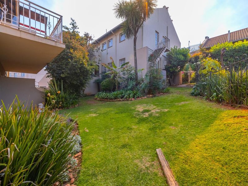 A rear view of the townhouse featuring a private garden, lawn area, and an external staircase leading to an upper-level balcony.