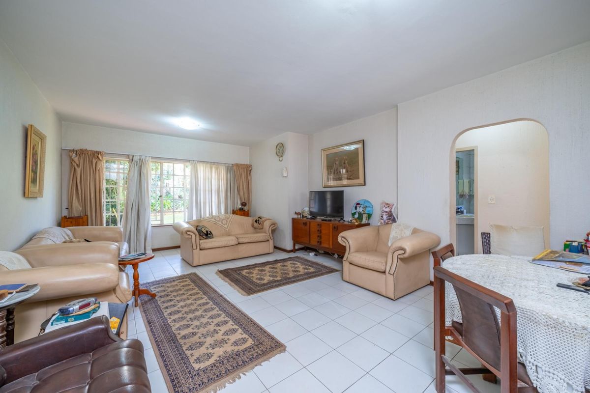 Spacious living room featuring tiled flooring, large windows allowing natural light, and an arched entryway leading to adjacent areas.