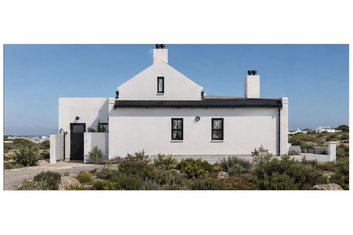A well-maintained white cottage-style house exterior featuring a dark metal roof, contrasting window frames, and a landscaped garden setting.