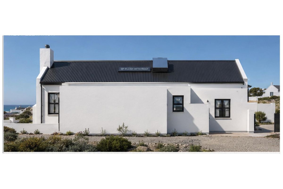 A well-maintained white cottage-style house featuring a dark corrugated metal roof, chimney, and solar water heating system.