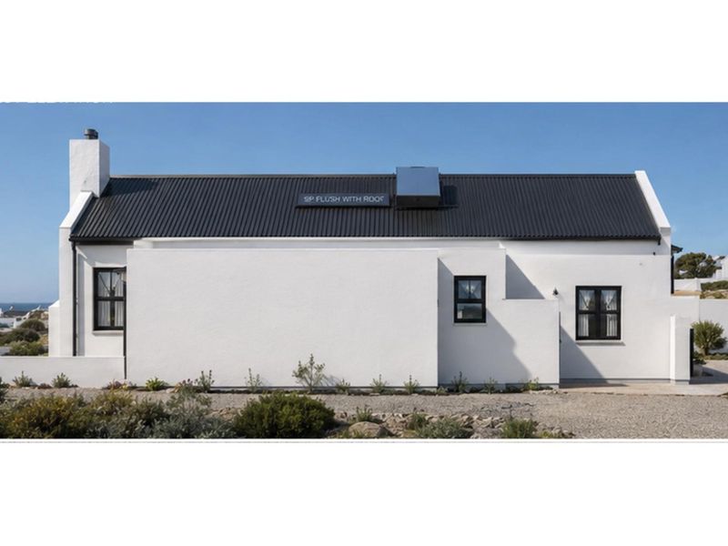 A well-maintained white cottage-style house featuring a dark corrugated metal roof, chimney, and solar water heating system.