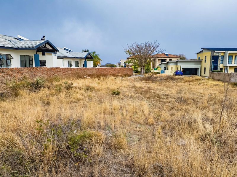 A vacant residential plot featuring dry, overgrown grass and enclosed by a brick boundary wall in a developed suburban neighborhood.