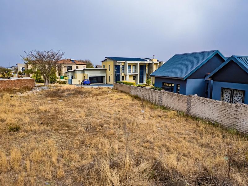 A view of a vacant residential plot featuring a boundary wall, situated in a developed neighborhood with surrounding residential properties.