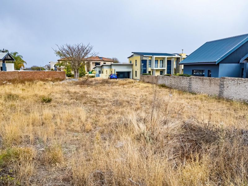 A vacant residential plot featuring dry grass and existing brick boundary walls, situated in a developed neighborhood.