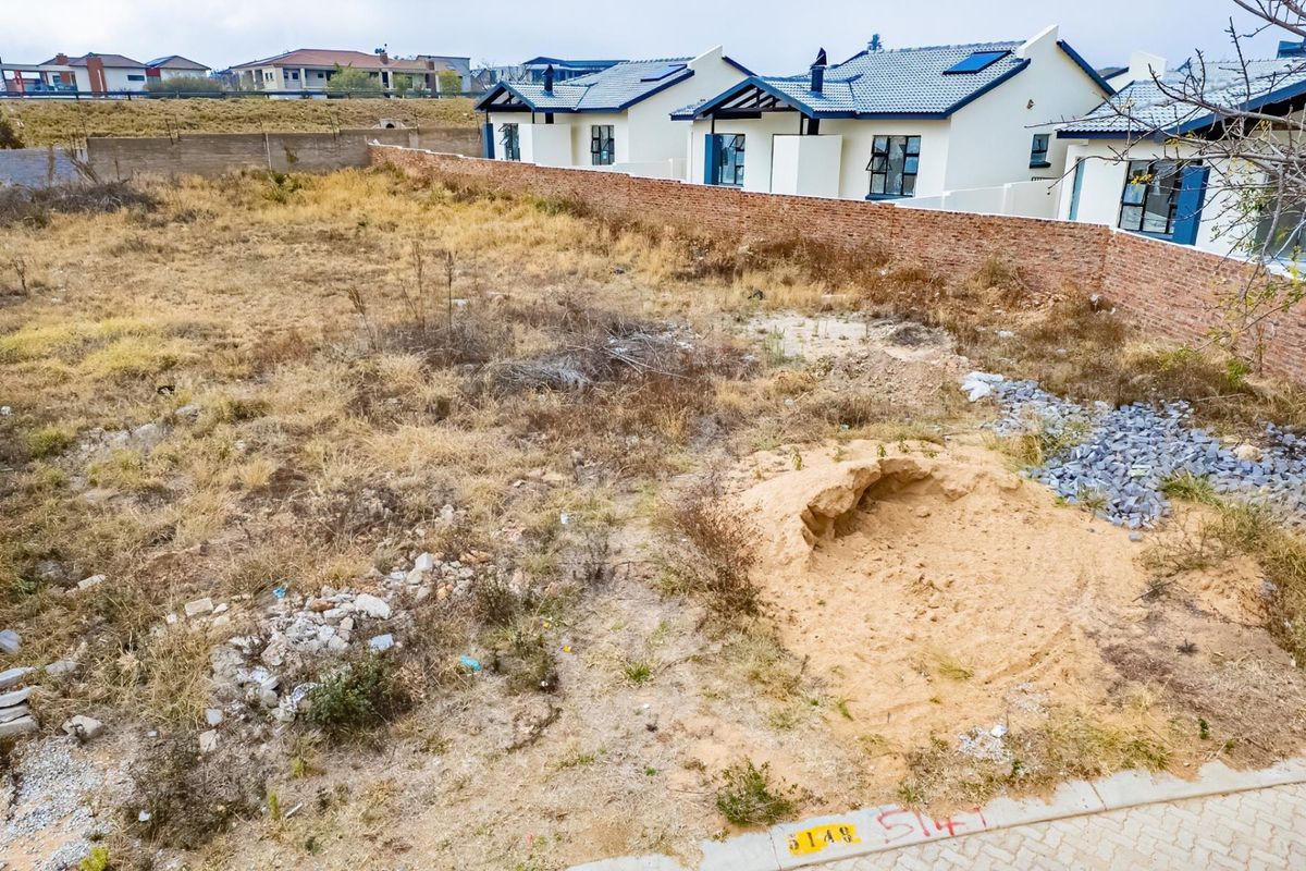 A vacant residential plot featuring a boundary wall and surrounding neighborhood development, offering a blank canvas for new construction.