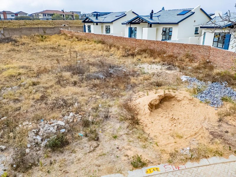 A vacant residential plot featuring a boundary wall and surrounding neighborhood development, offering a blank canvas for new construction.