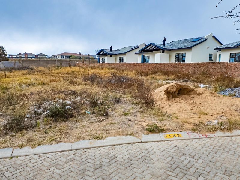 A vacant residential plot featuring a paved street frontage and a brick boundary wall, ready for development in an established neighborhood.