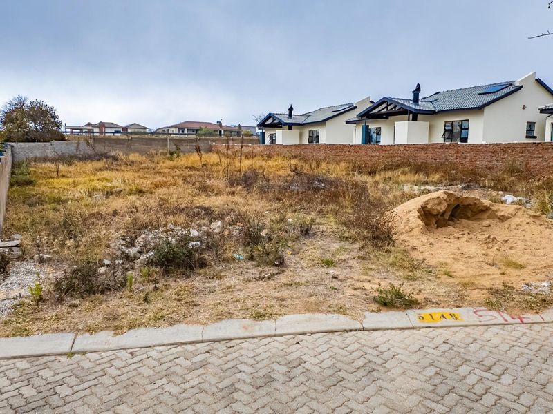 A vacant residential plot featuring a paved street frontage and perimeter brick walling, ready for development.