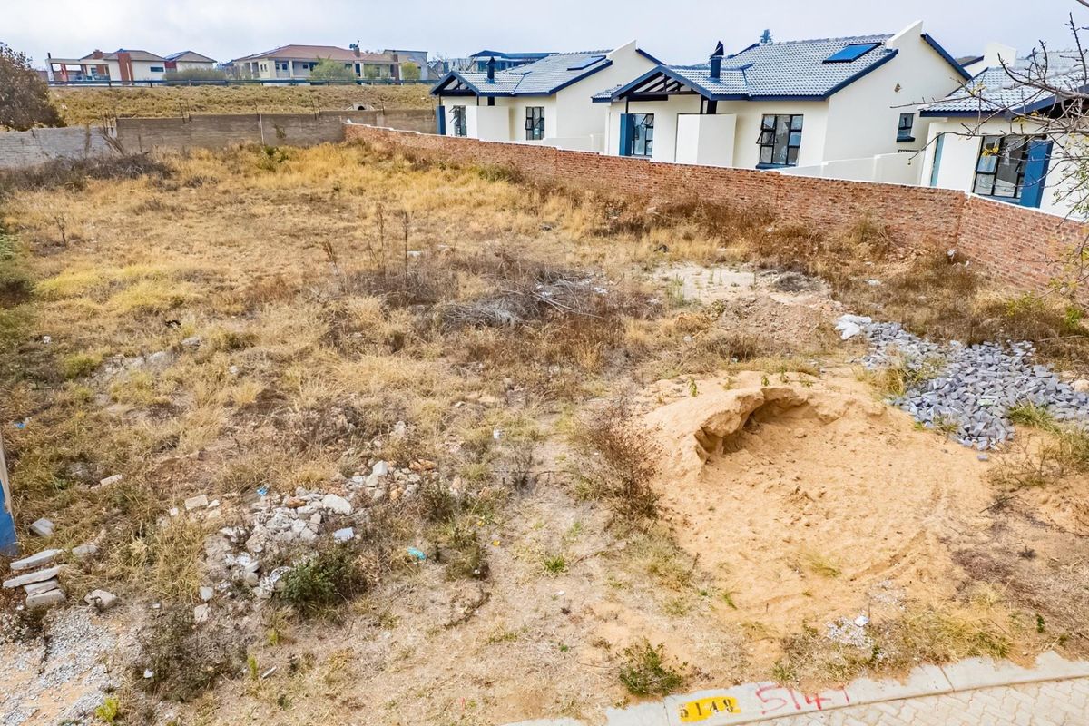 A vacant residential plot featuring a brick boundary wall and natural vegetation, situated in a developed neighborhood.