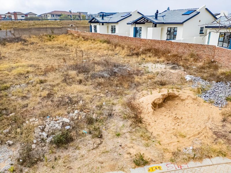 A vacant residential plot featuring a brick boundary wall and natural vegetation, situated in a developed neighborhood.